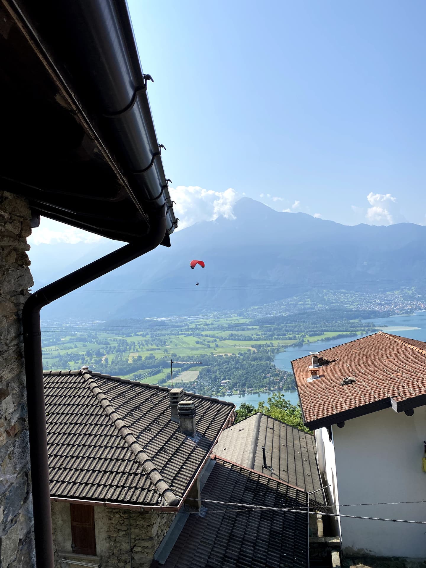 Paraglider svever over dalen, sett fra husets takskjegg